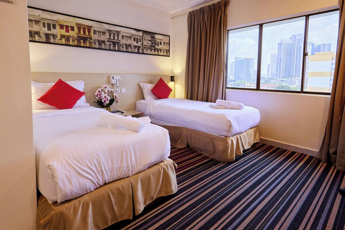 Ein Hotelzimmer mit zwei Betten, Blick auf die Stadt, einem gerahmten Bild an der Wand und einem Streifenmuster-Teppich.