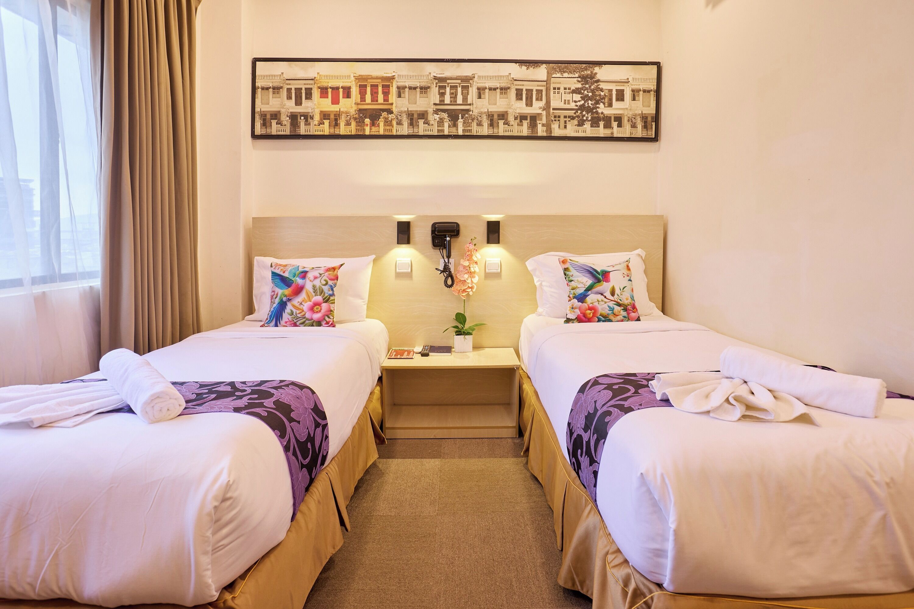 A hotel room with two beds, a nightstand with a lamp, a framed picture on the wall, and a window with curtains.
