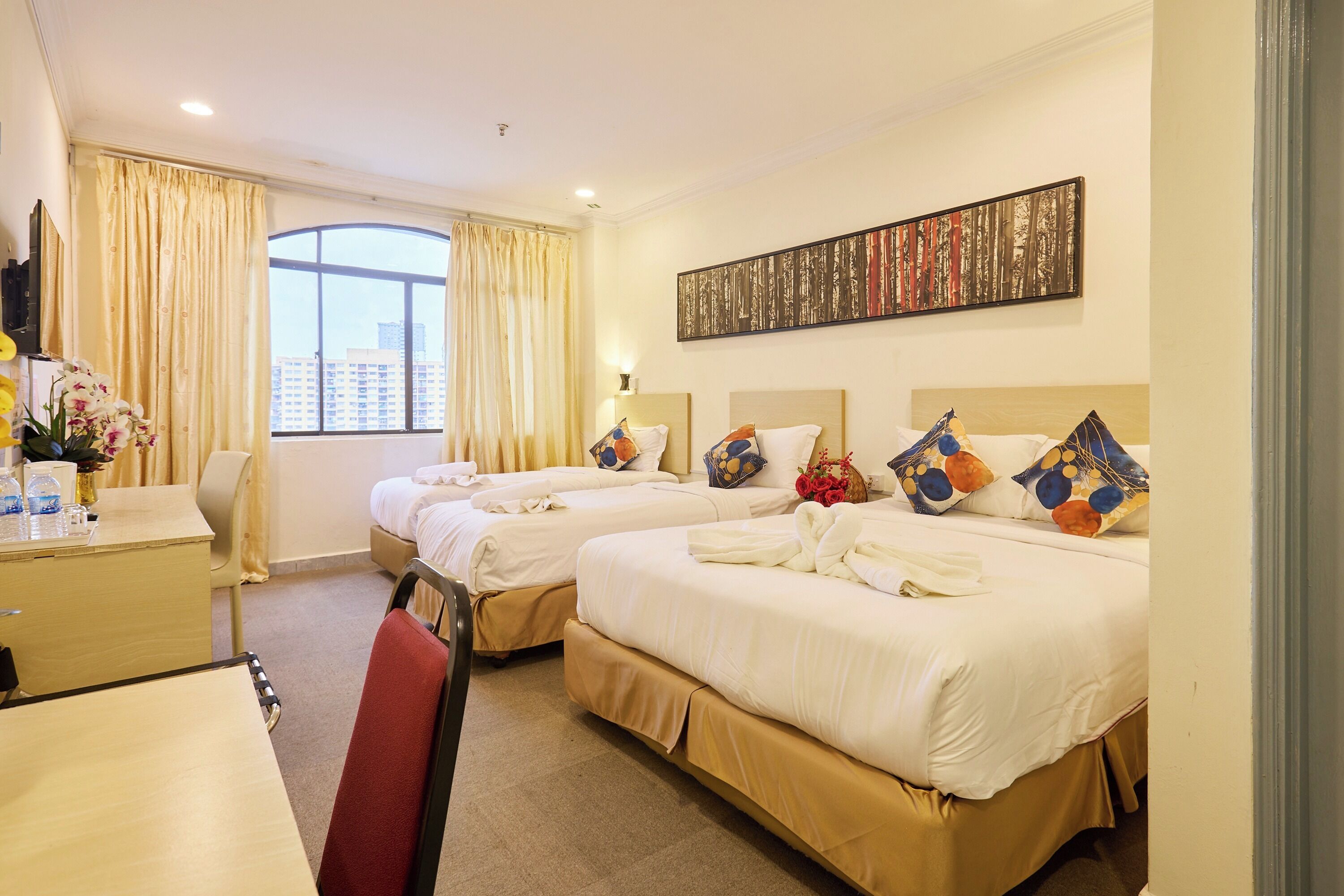 A hotel room with two beds, a desk, a chair, a window with curtains, and a painting on the wall.