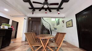 A wooden dining table with four chairs, a ceiling fan, and a staircase in the background. - Bangera Inn (Puerto Galera)