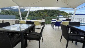 An outdoor dining area with tables and chairs, a white canopy, and a view of a green hillside. - Bangera Inn (Puerto Galera)