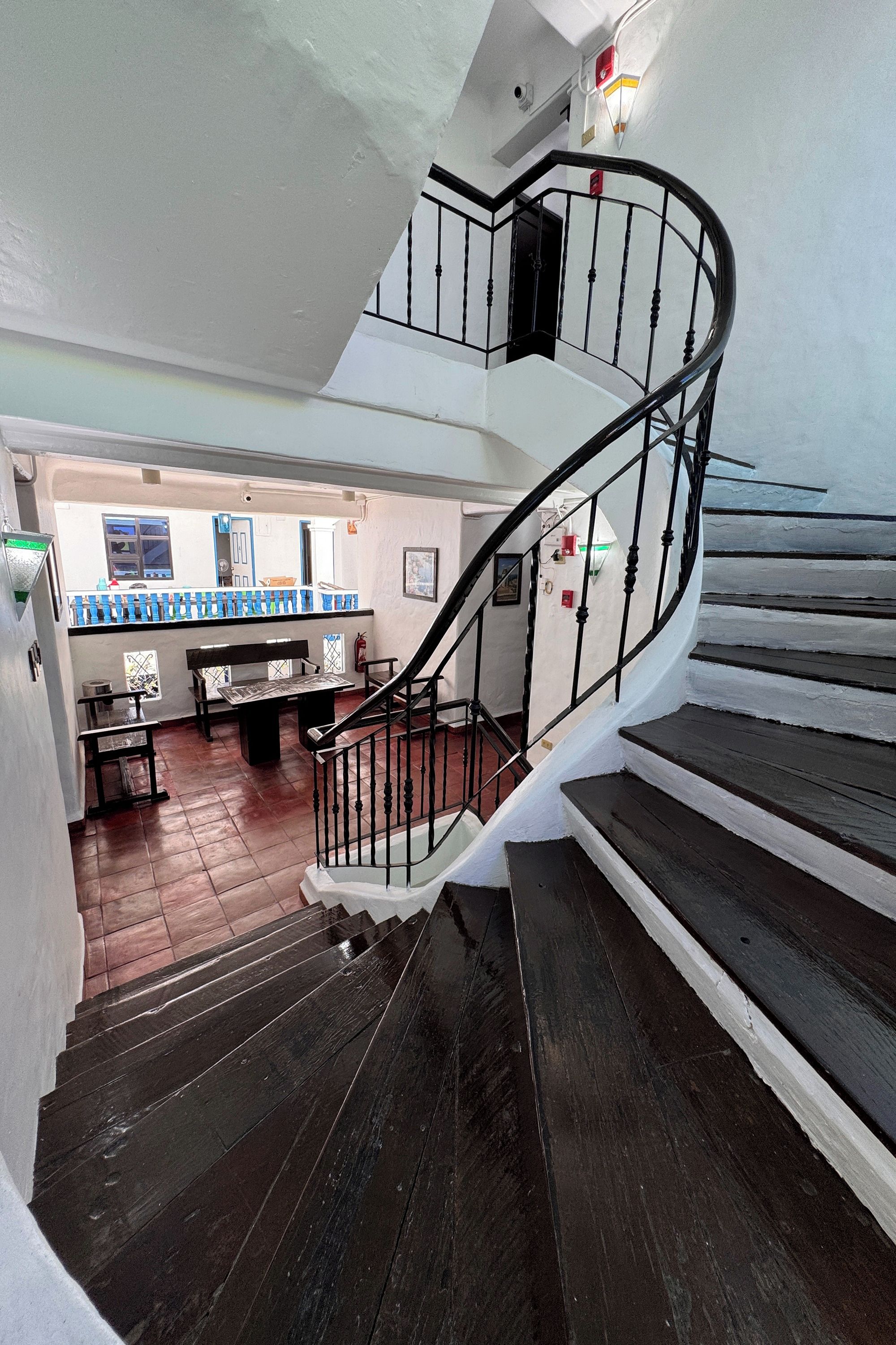 Una escalera en espiral con escalones de madera oscura y barandillas de metal negro que conducen a un piso superior.