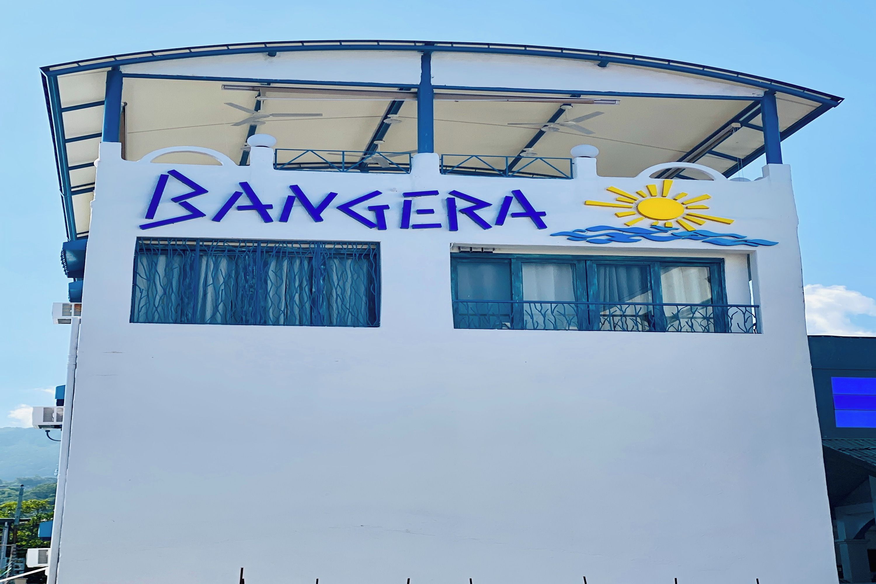 Un bâtiment sur lequel on peut lire l’inscription « BANGERA » et qui arbore un symbole solaire, ce qui indique qu’il s’agit d’un hôtel ou d’un complexe touristique.