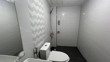 A small, modern bathroom with a toilet, bidet, and shower.