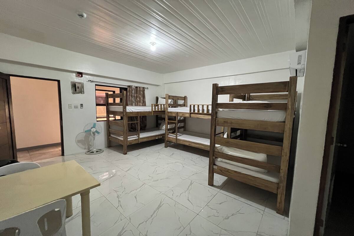 Una camera del dormitorio con letti a castello, una ventola, un tavolo e una porta.