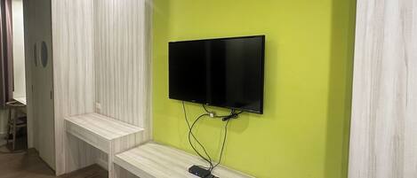 Quarto moderno com televisão de tela plana fixada em parede verde, um banco de madeira e uma porta com janela circular.