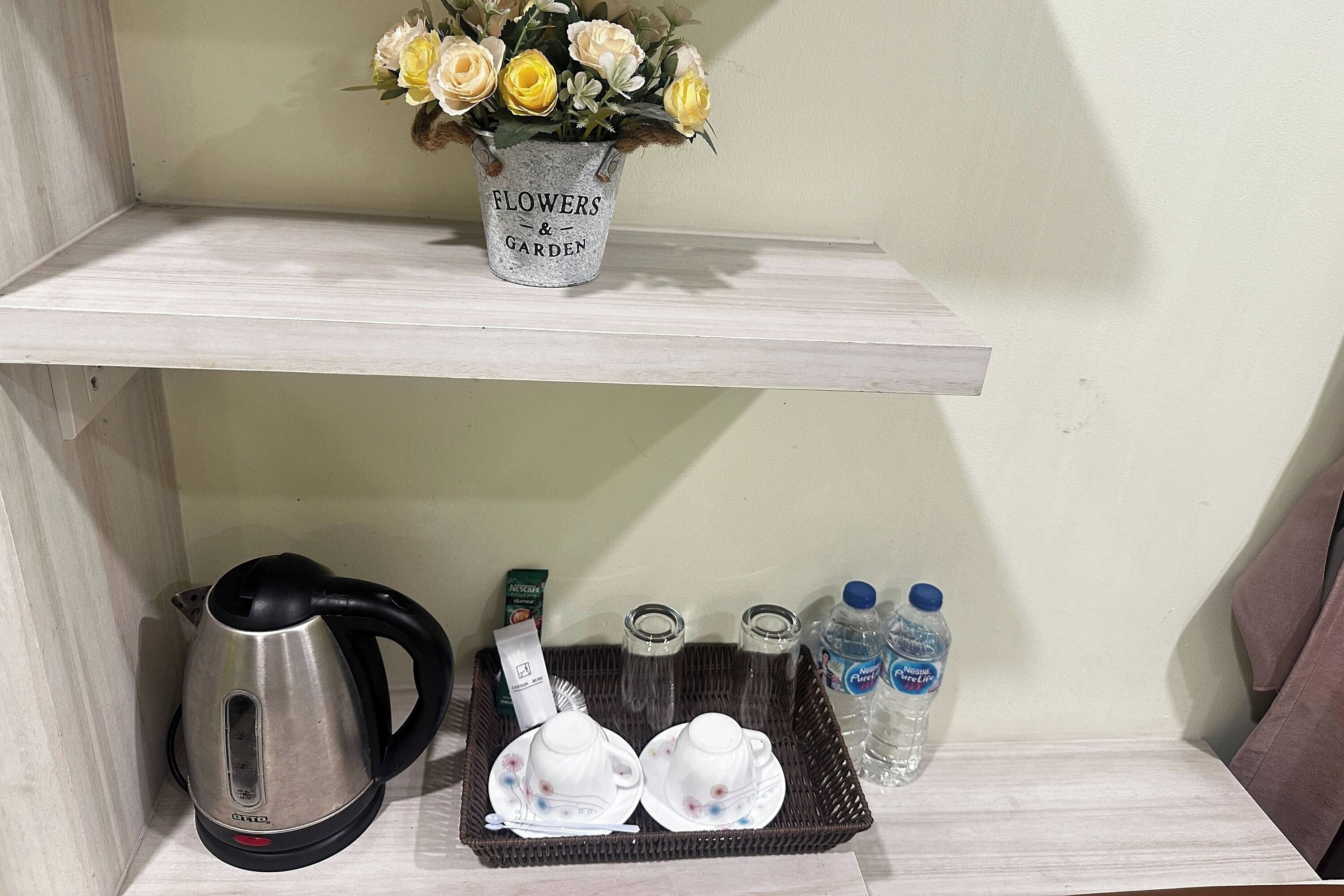 A shelf with a flower vase, a kettle, a tray with teacups, and water bottles.