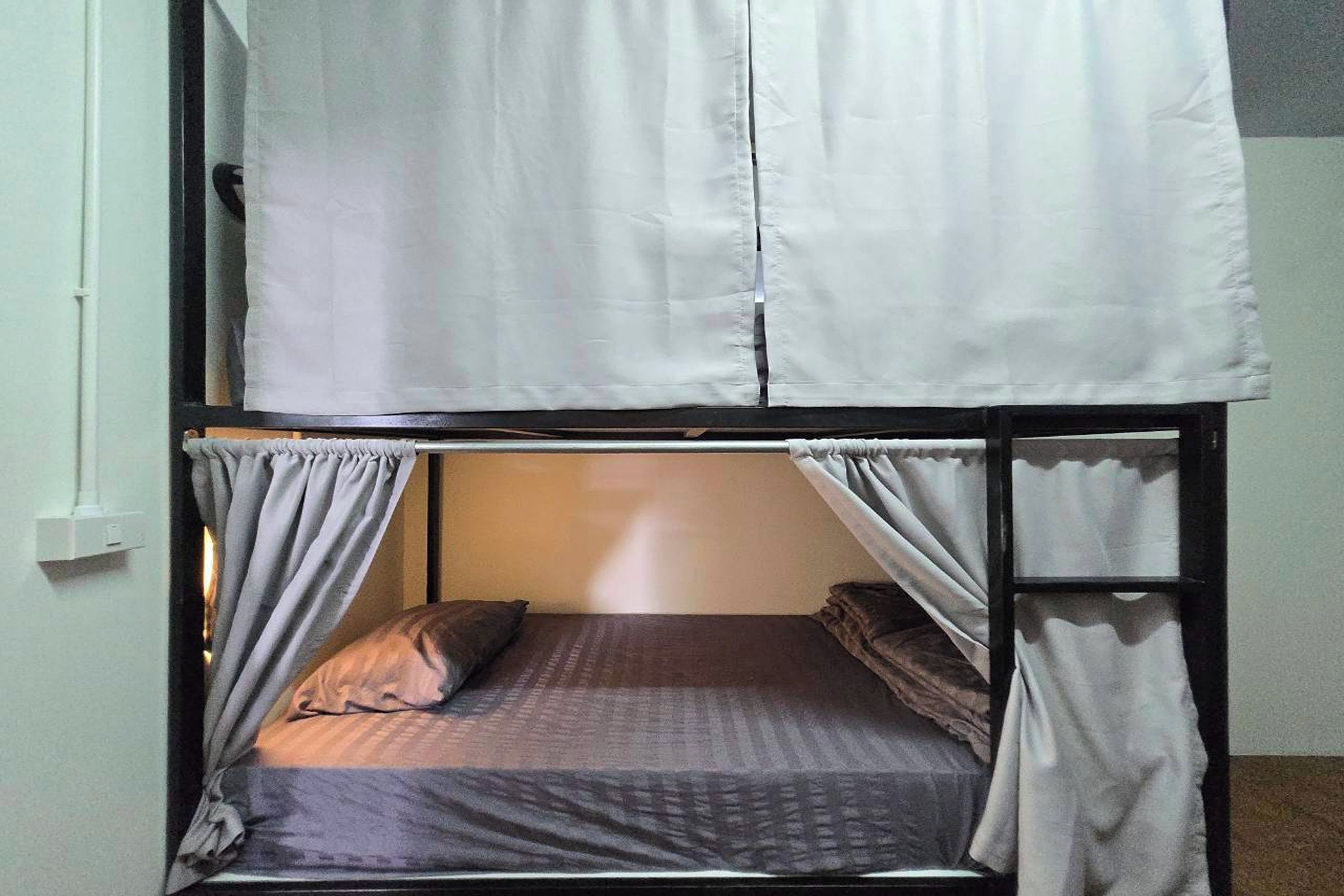 A bunk bed with a headboard, curtains, and a mattress with pillows.