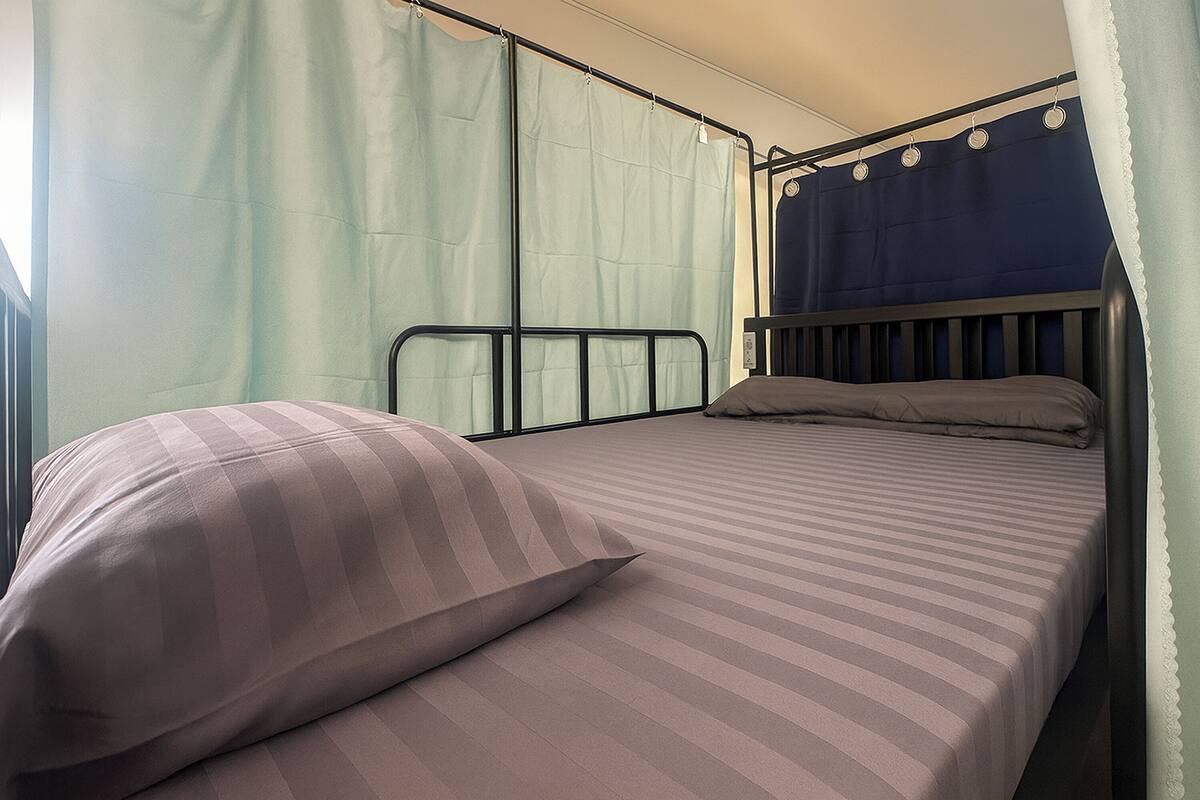A single bed with a striped mattress and a pillow, a window with a curtain, and a headboard with a clock.