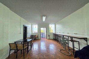A spacious room with a wooden floor, a dining table with chairs, a bar area with stools, and a large window providing natural light. - Hostel Happy Elephant (Chiang Mai)