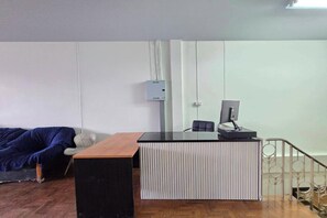 A reception desk with a computer, a chair, and a blue couch in a room with white walls and a wooden floor. - Hostel Happy Elephant (Chiang Mai)