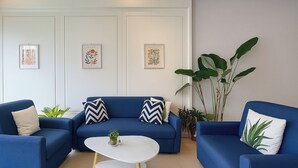Un salon moderne avec un canapé bleu, des murs blancs et des œuvres d’art encadrées.