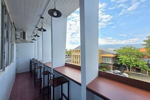 A balcony with a row of bar stools, a white railing, and a view of the street and buildings. - Hostel Happy Elephant (Chiang Mai)