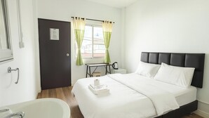 Ein Hotelzimmer mit Bett, Nachttisch, Fenster mit Vorhängen, Waschbecken und Tür.