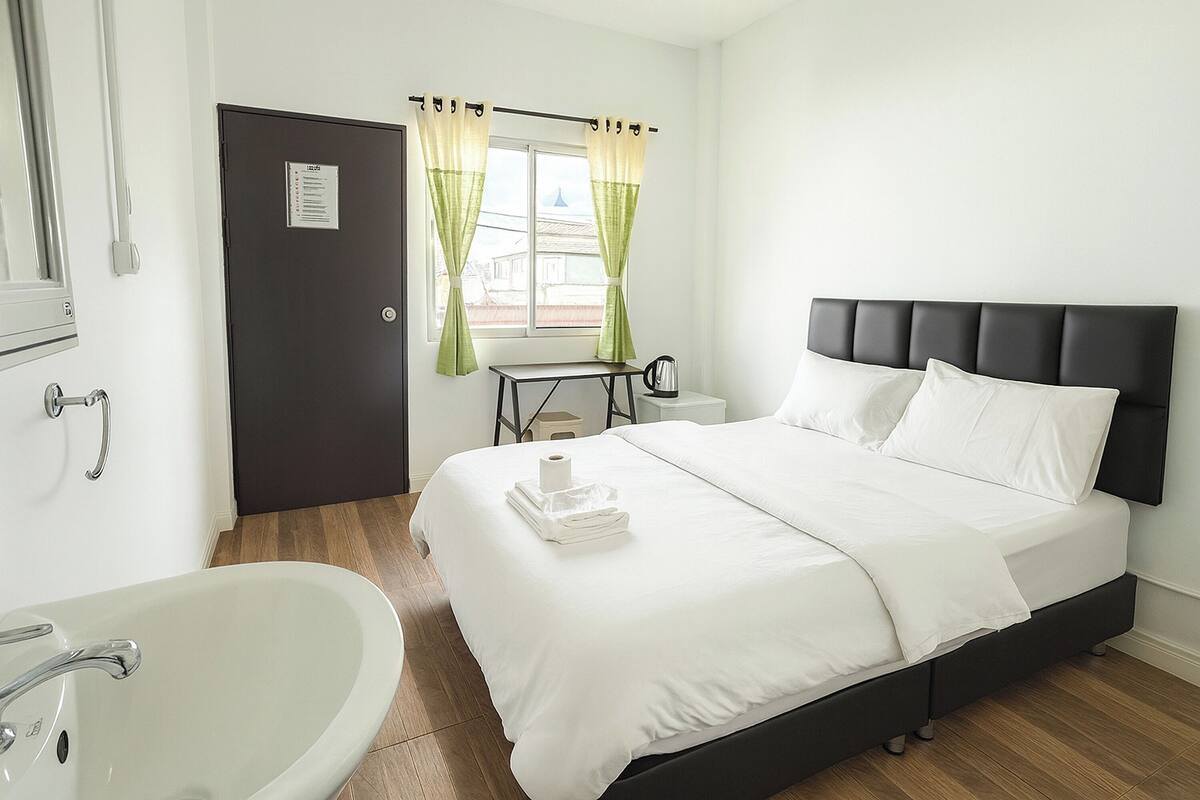 Een hotelkamer met een bed, een nachtkastje, een raam met gordijnen, een wastafel en een deur.