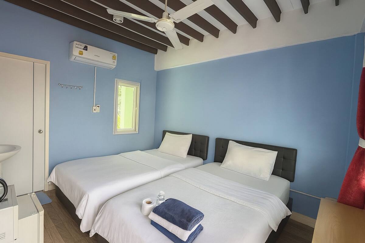 Hotelkamer met twee bedden, een plafondventilator, een airconditioning, een raam en een badkamer met een wastafel en spiegel.