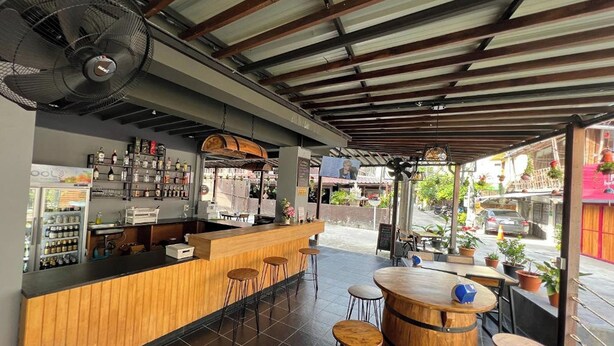 Eine Bar mit einer Holztresen, Hockstühlen und einem Ventilator.
