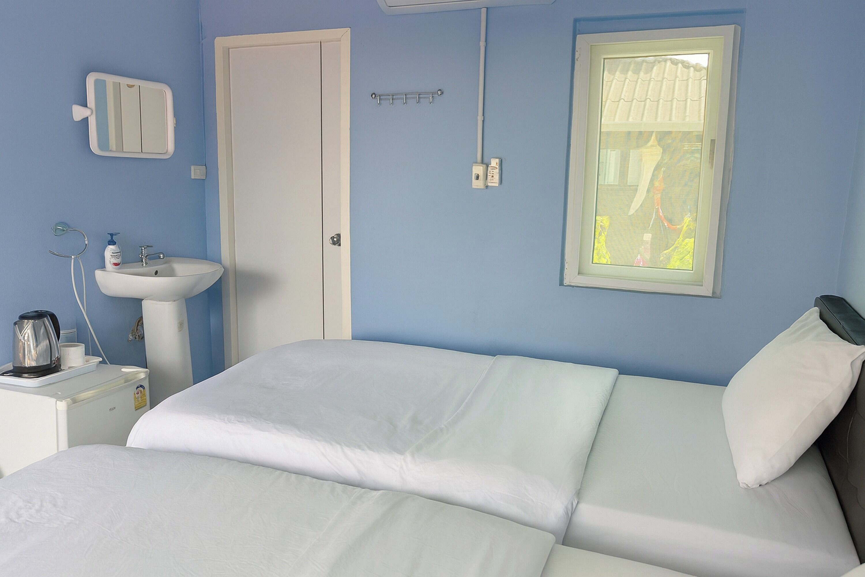 Une chambre à coucher avec un lit, une table de chevet avec une lampe, une fenêtre et une salle de bain avec un lavabo et un miroir.