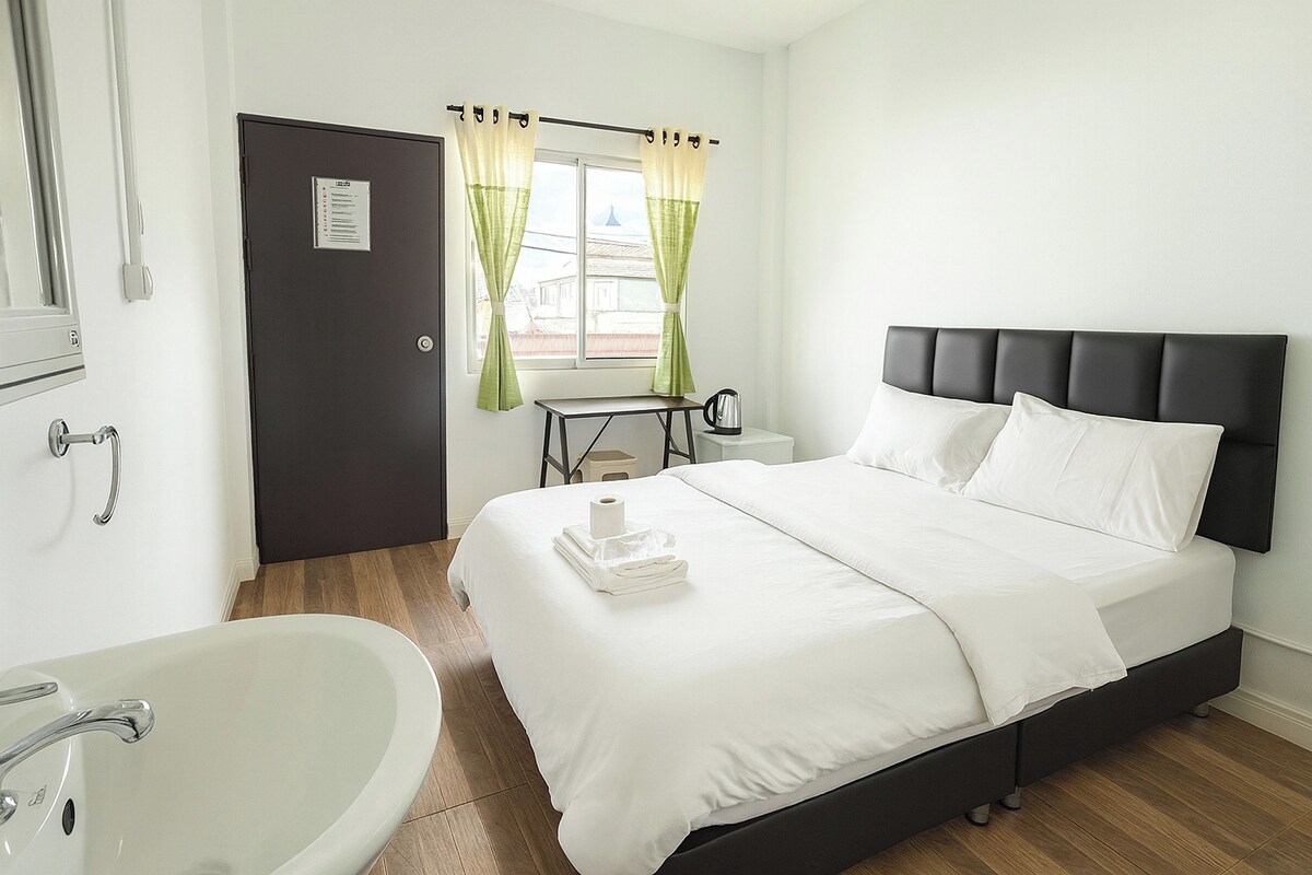 Une chambre d’hôtel avec un lit, une table de chevet, une fenêtre avec des rideaux, un lavabo et une porte.