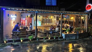 Ein Straßencafé mit Tischen, Stühlen und Topfpflanzen, sowie ein Neon-Schild.