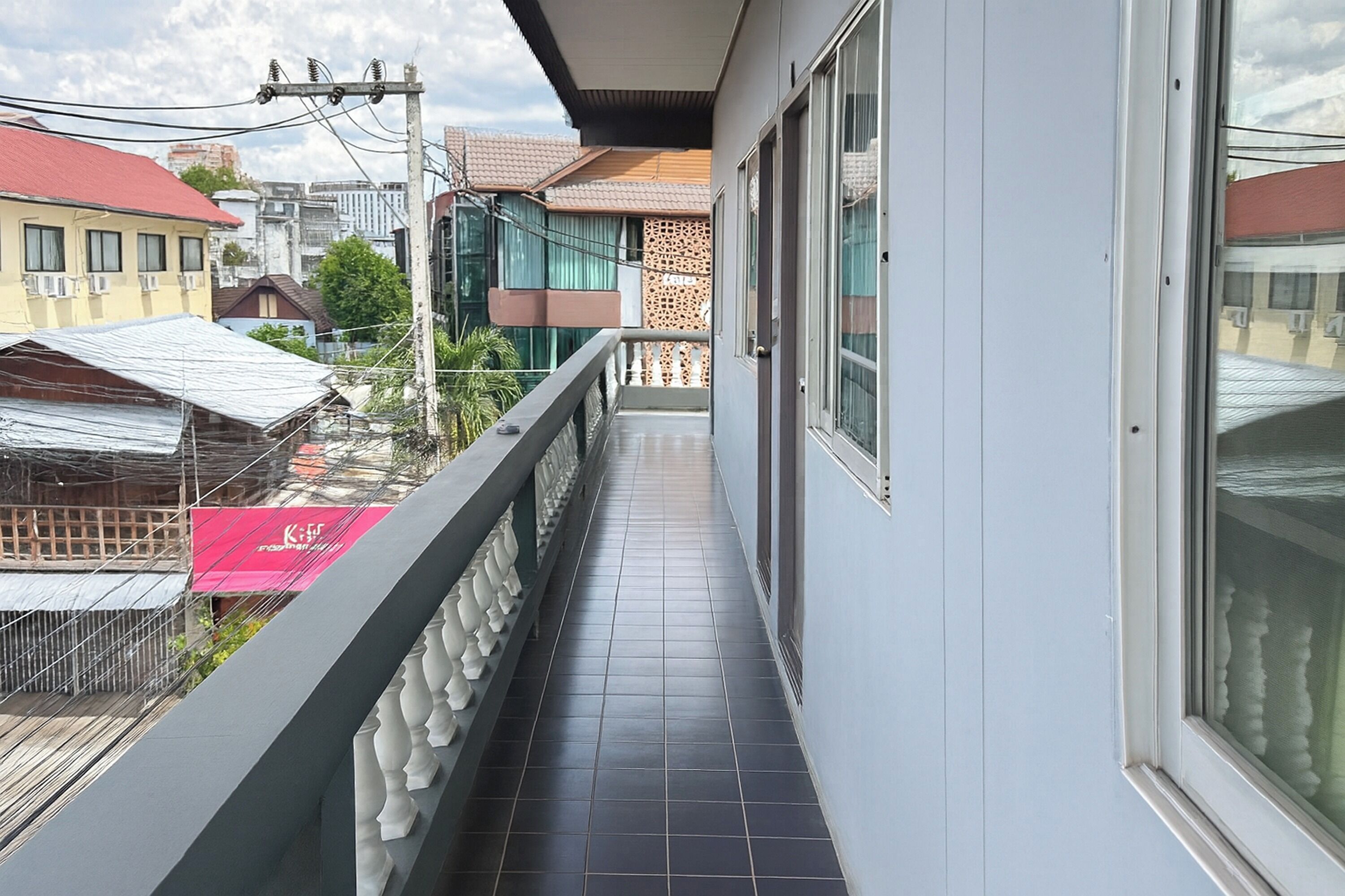 A narrow balcony with a tiled floor, a railing with decorative elements, and a view of neighboring buildings.