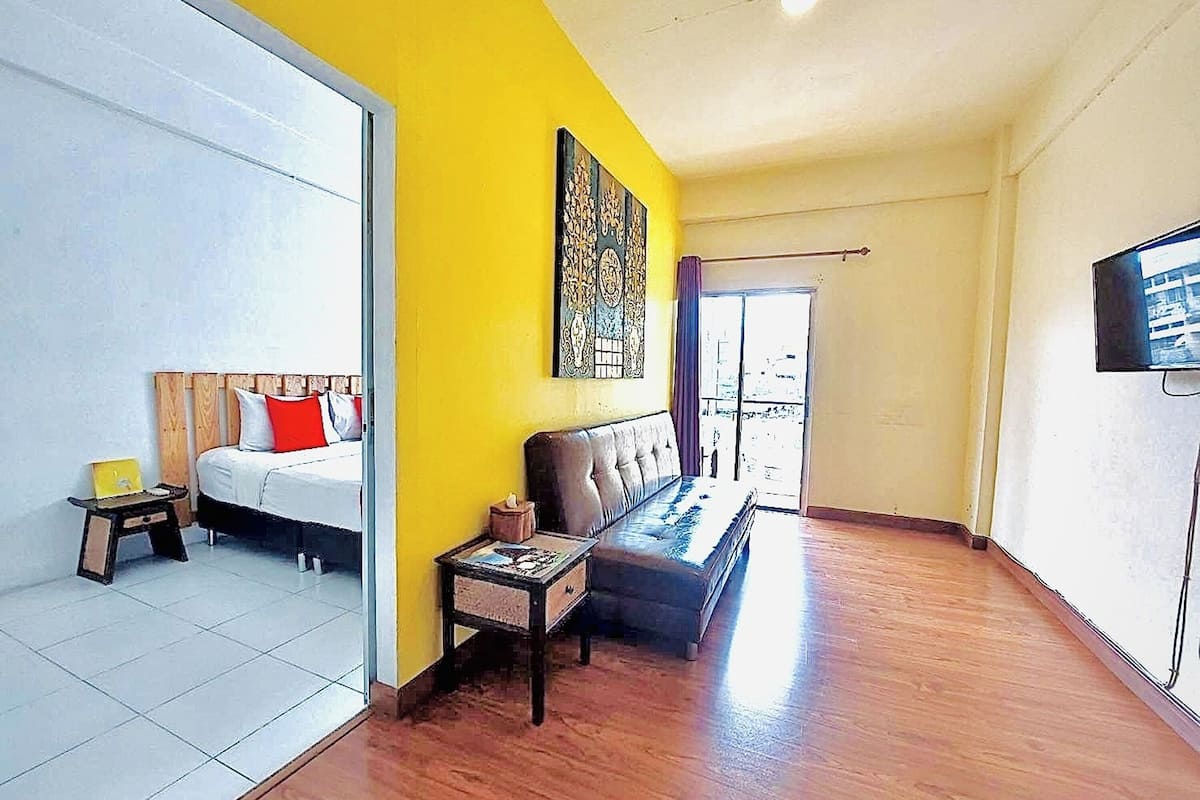 Una habitación de hotel con cama, sofá, mesita, televisor y ventana grande.