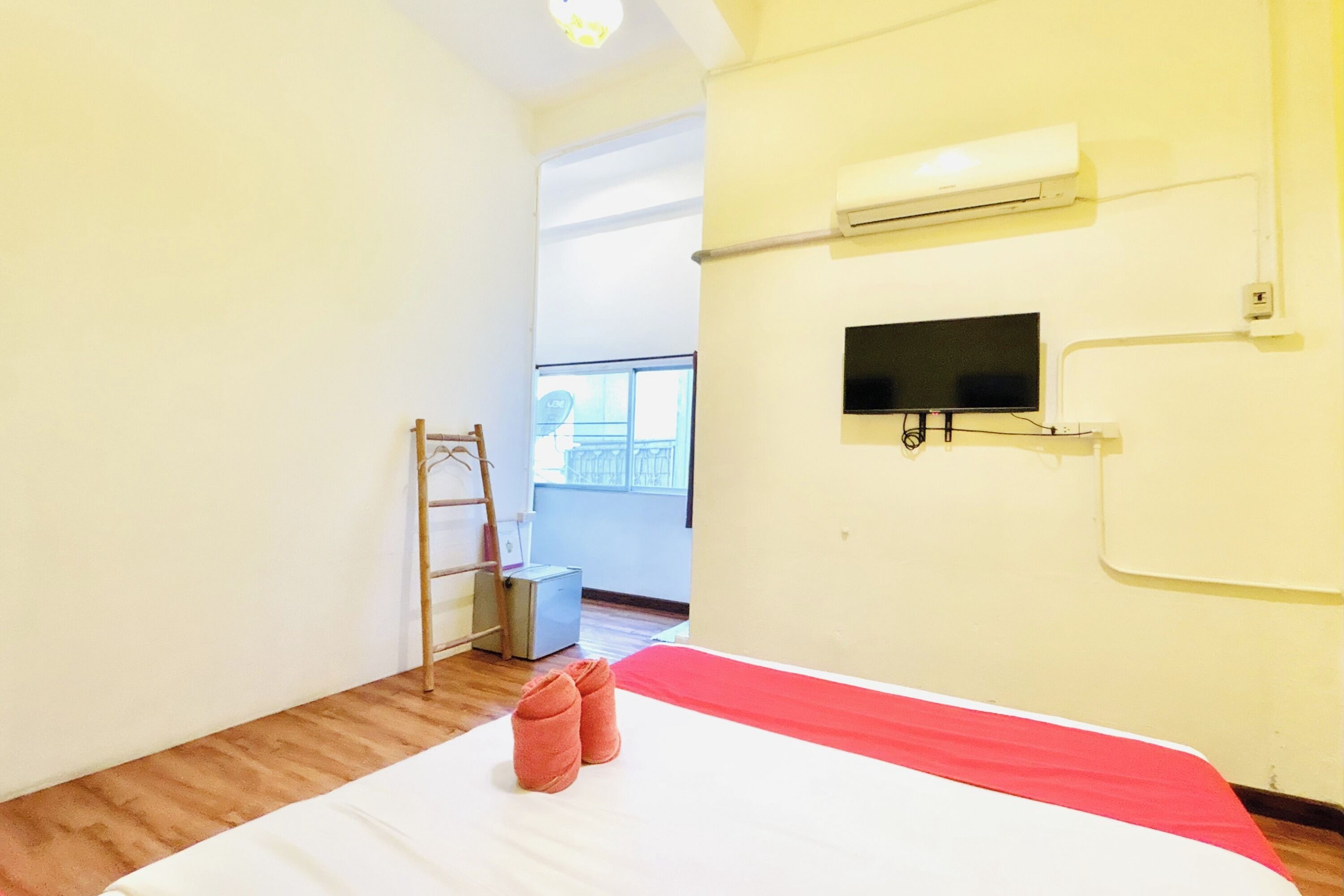 A bedroom with a bed, a TV, an air conditioner, a ladder, and a window.