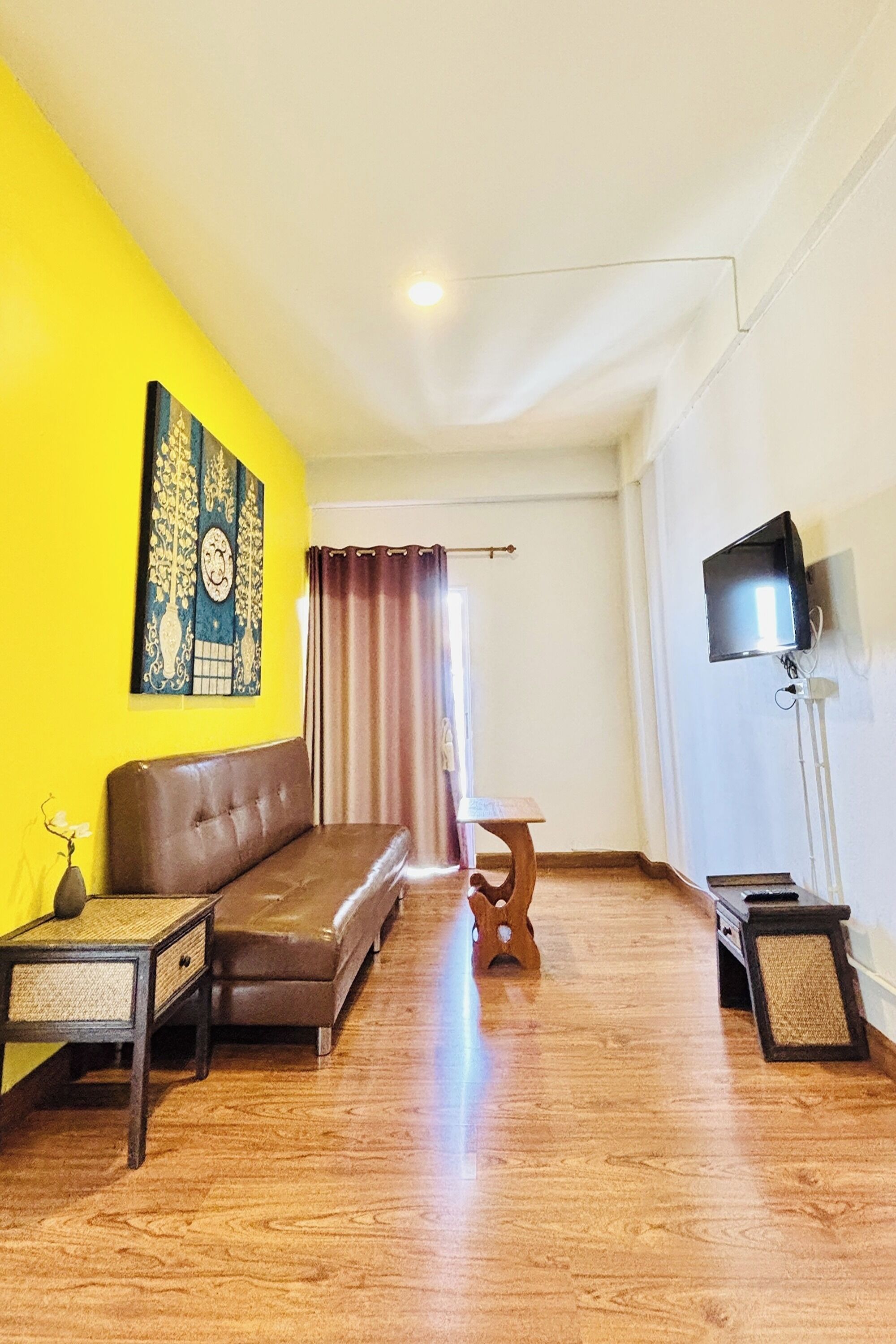 Um quarto com um sofá de couro marrom, uma mesa de madeira pequena, uma televisão em um suporte e um quadro na parede.