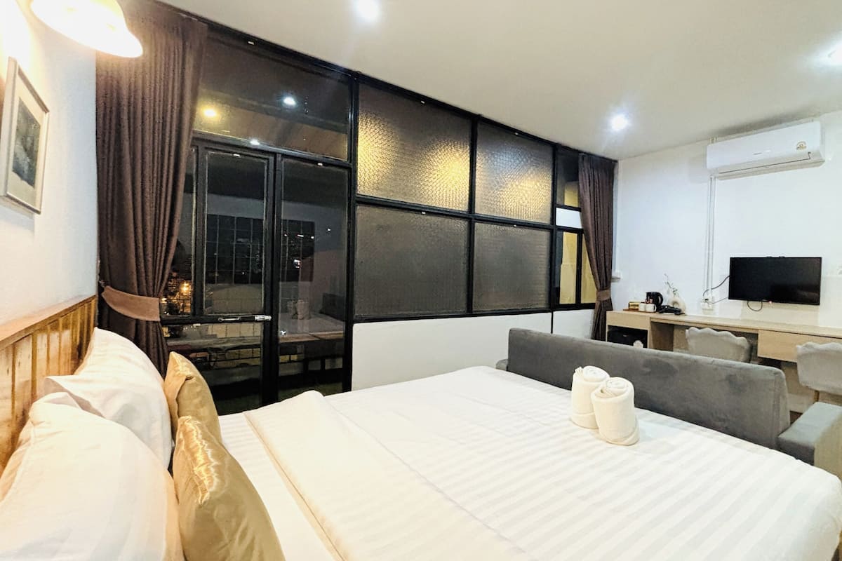 Una habitación de hotel con cama, escritorio, silla, televisor y ventana con cortinas.