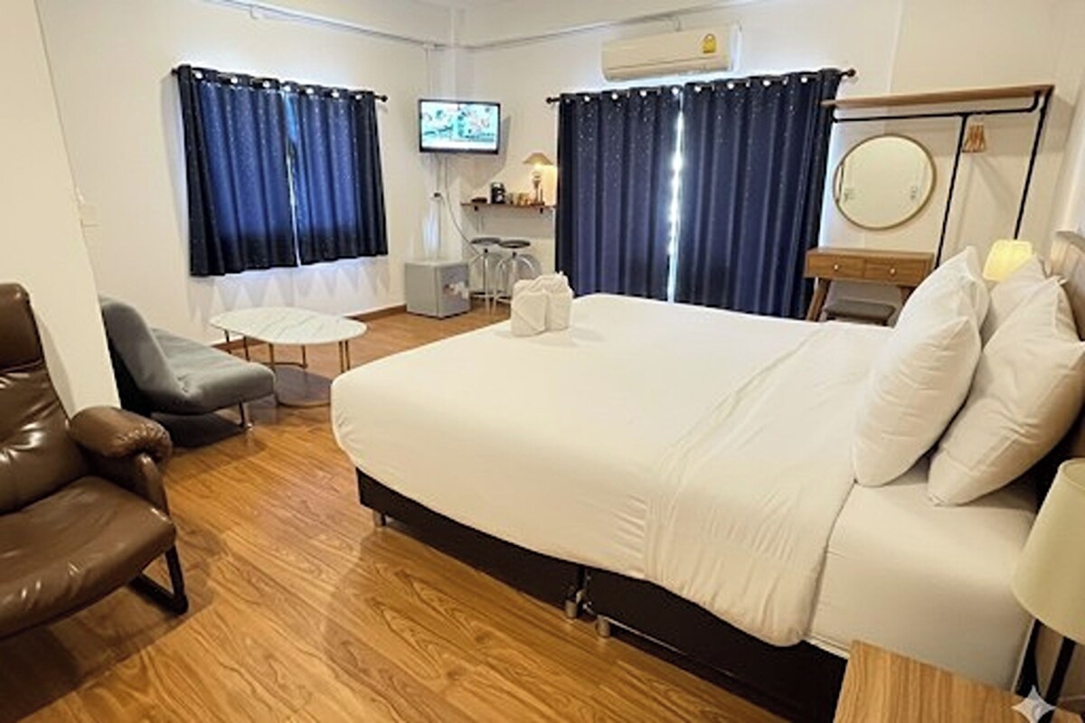 Une chambre d’hôtel avec un lit, un canapé, une petite table, une télévision, un miroir et des rideaux.