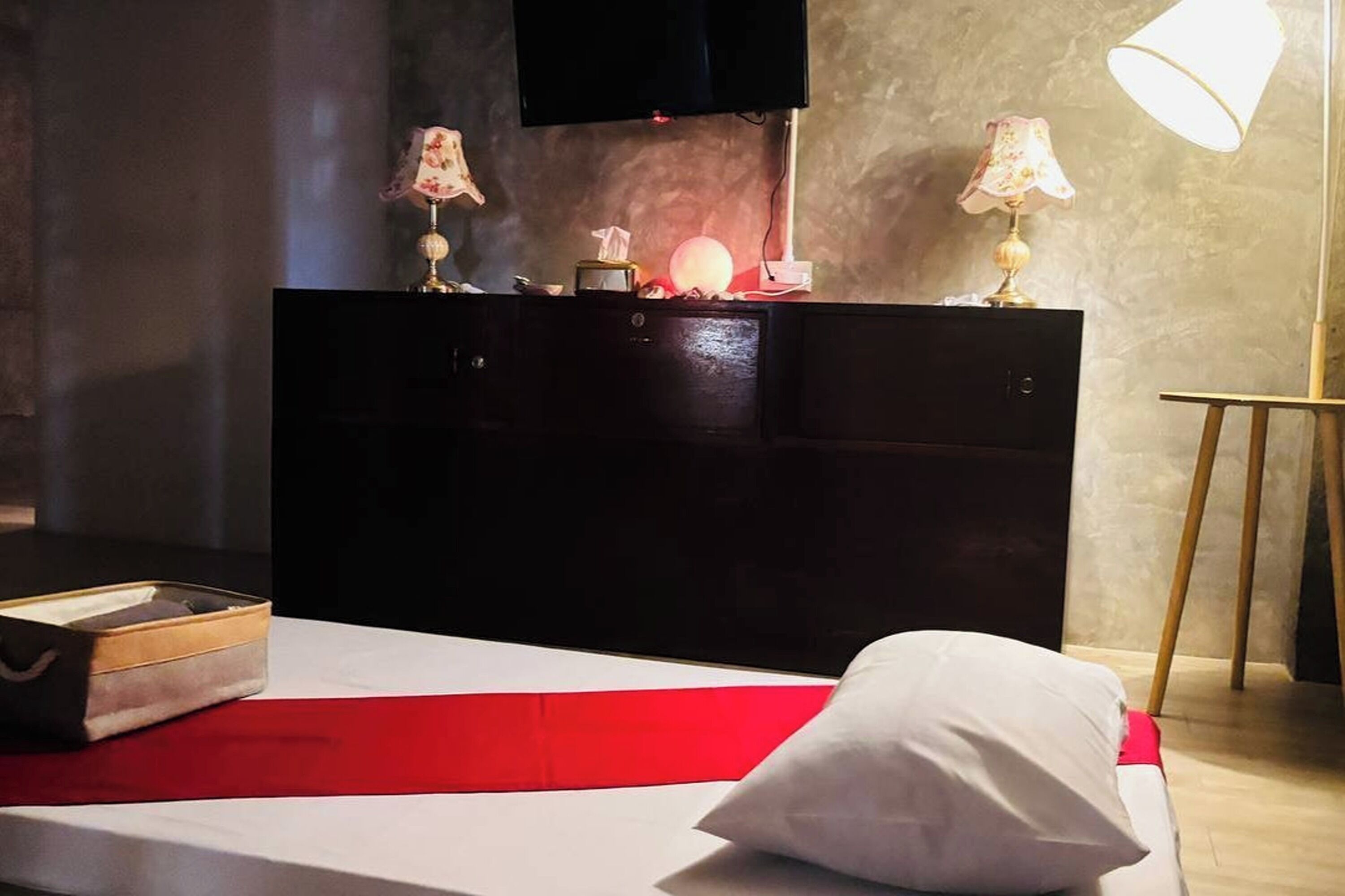A hotel room with a bed, a bedside table with lamps, a TV mounted on the wall, and a bedside lamp.