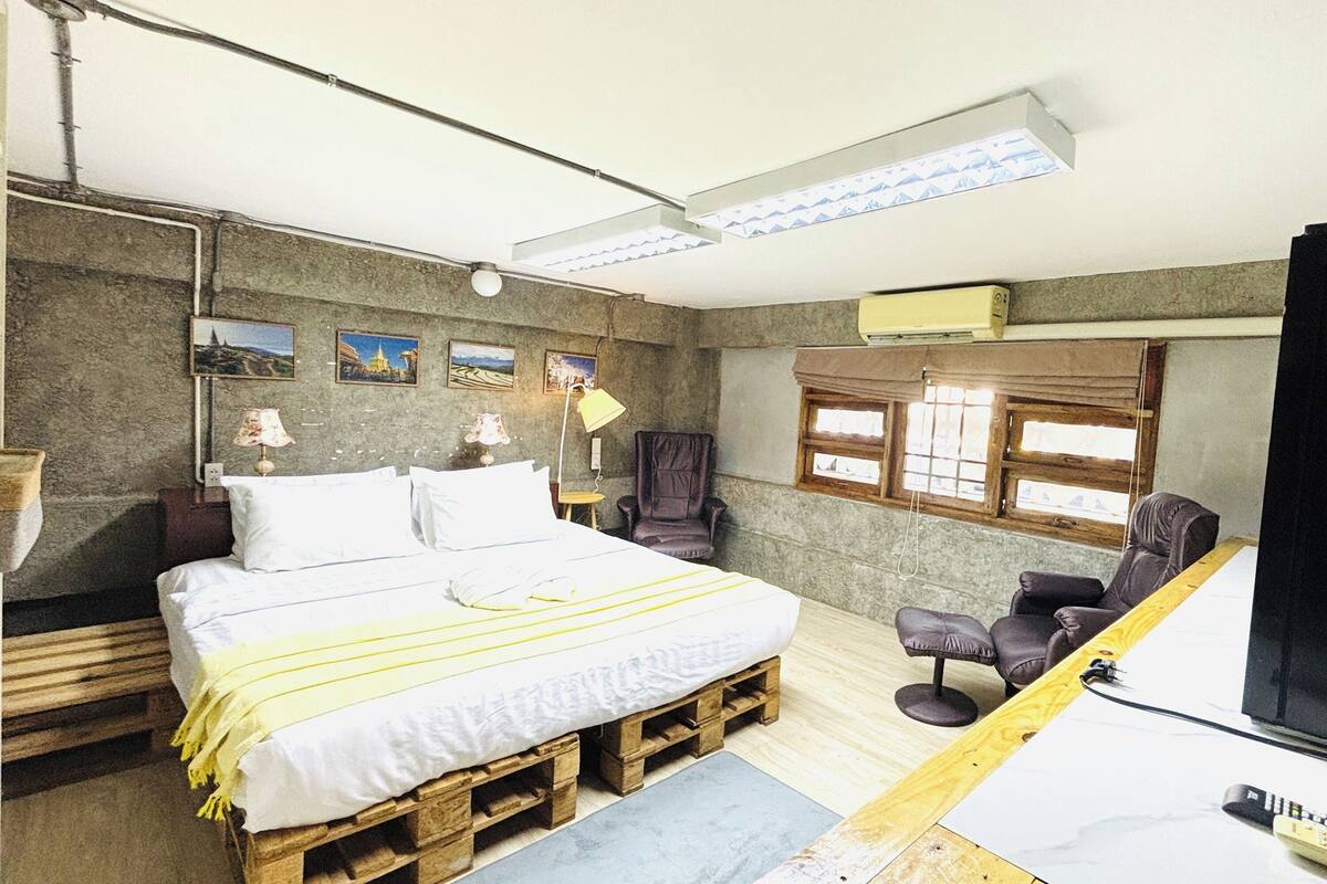 Una habitación con una cama sobre palets de madera, un escritorio, una silla y un televisor.