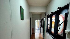 Un couloir au sol carrelé, aux murs blancs, et orné d’œuvres d’art sur le côté droit.