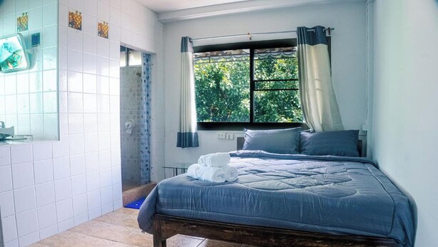 Une chambre avec un lit, une fenêtre avec des rideaux, un espace douche et un mur carrelé.