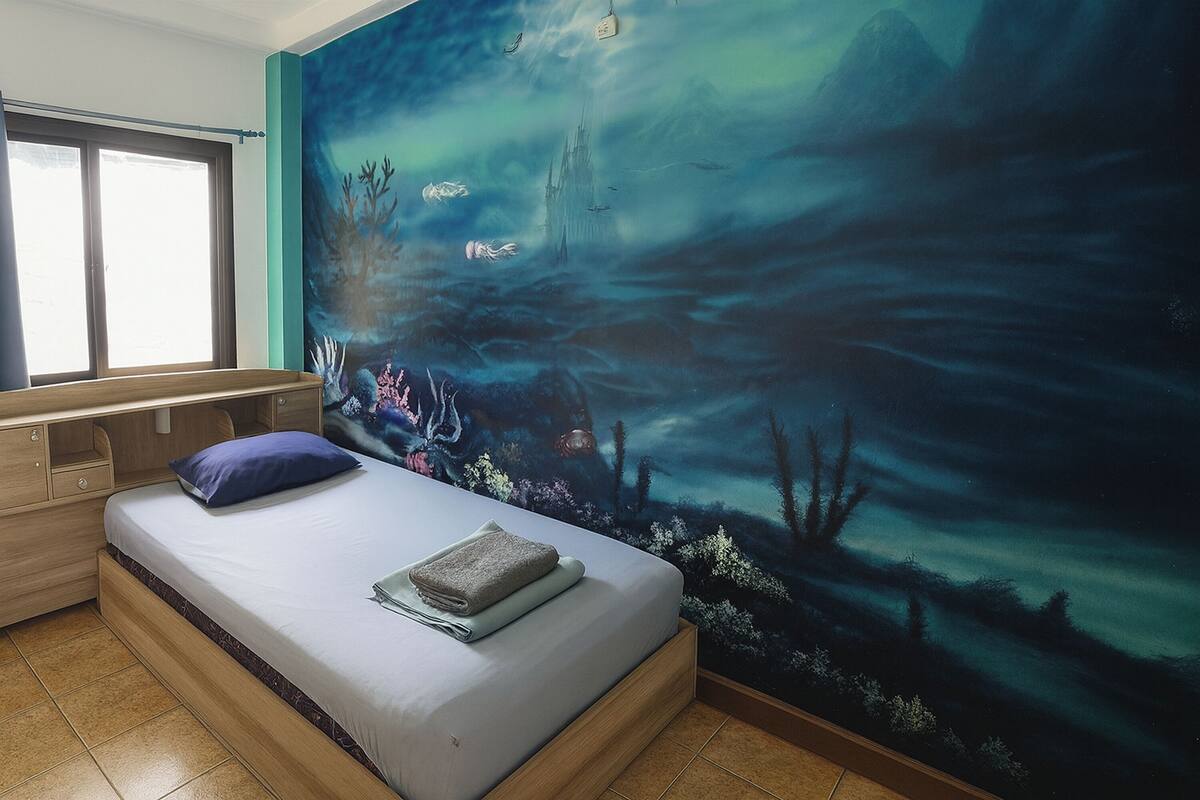 Une chambre à coucher avec un lit, une fenêtre et une fresque représentant un paysage sous-marin.
