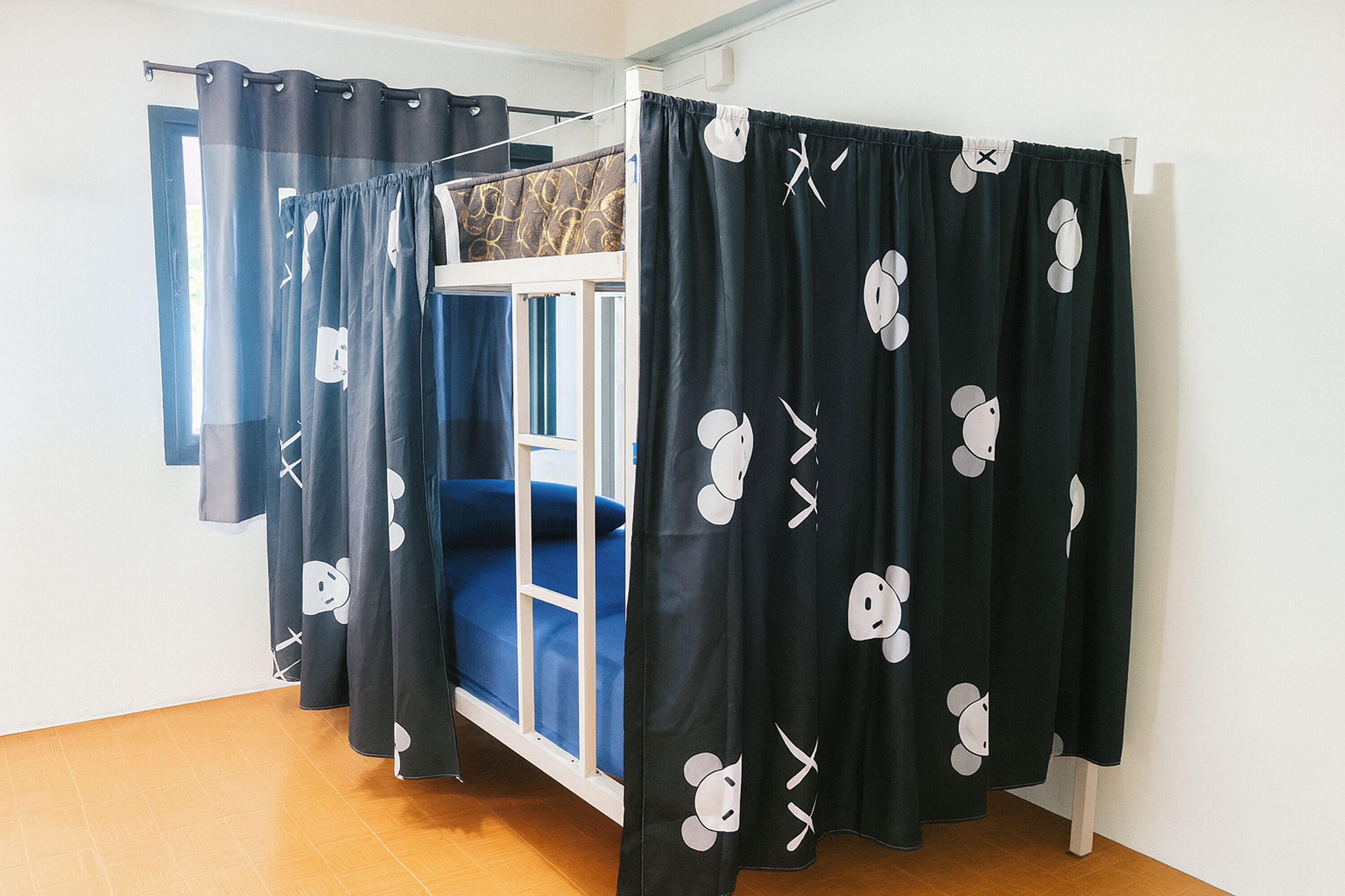 Une chambre avec un lit superposé, des rideaux noirs ornés de personnages de dessins animés et un plancher en bois.