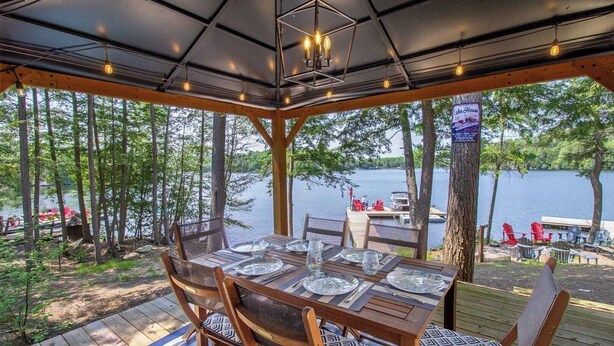 A covered outdoor dining area with a table set for four, overlooking a lake with docked boats and chairs. - Steenburg Shores & S'mores (Gilmour)