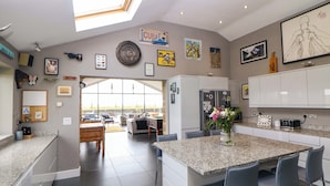 A modern kitchen with a central island, bar stools, and a dining area with a view. - Highgate House (Dronfield)