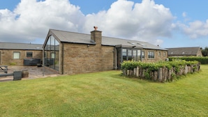 A stone building with a glass conservatory, a grassy lawn, and a wooden fence. - Highgate House (Dronfield)