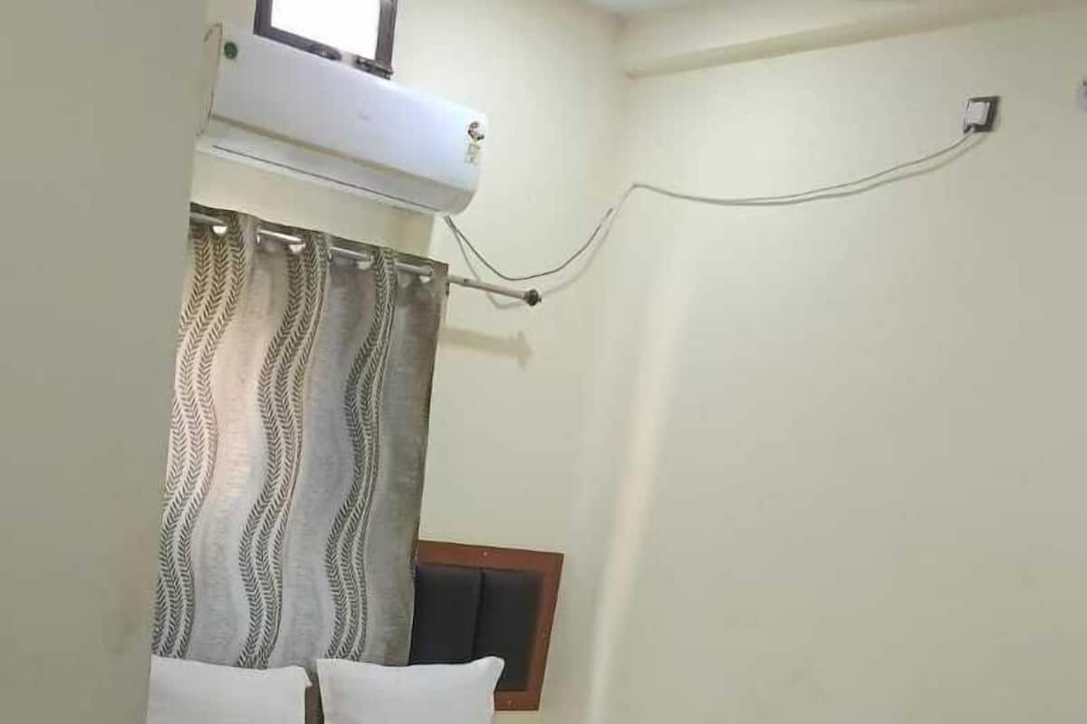 A small, neatly arranged bedroom with a bed, a ceiling fan, and a window with curtains.