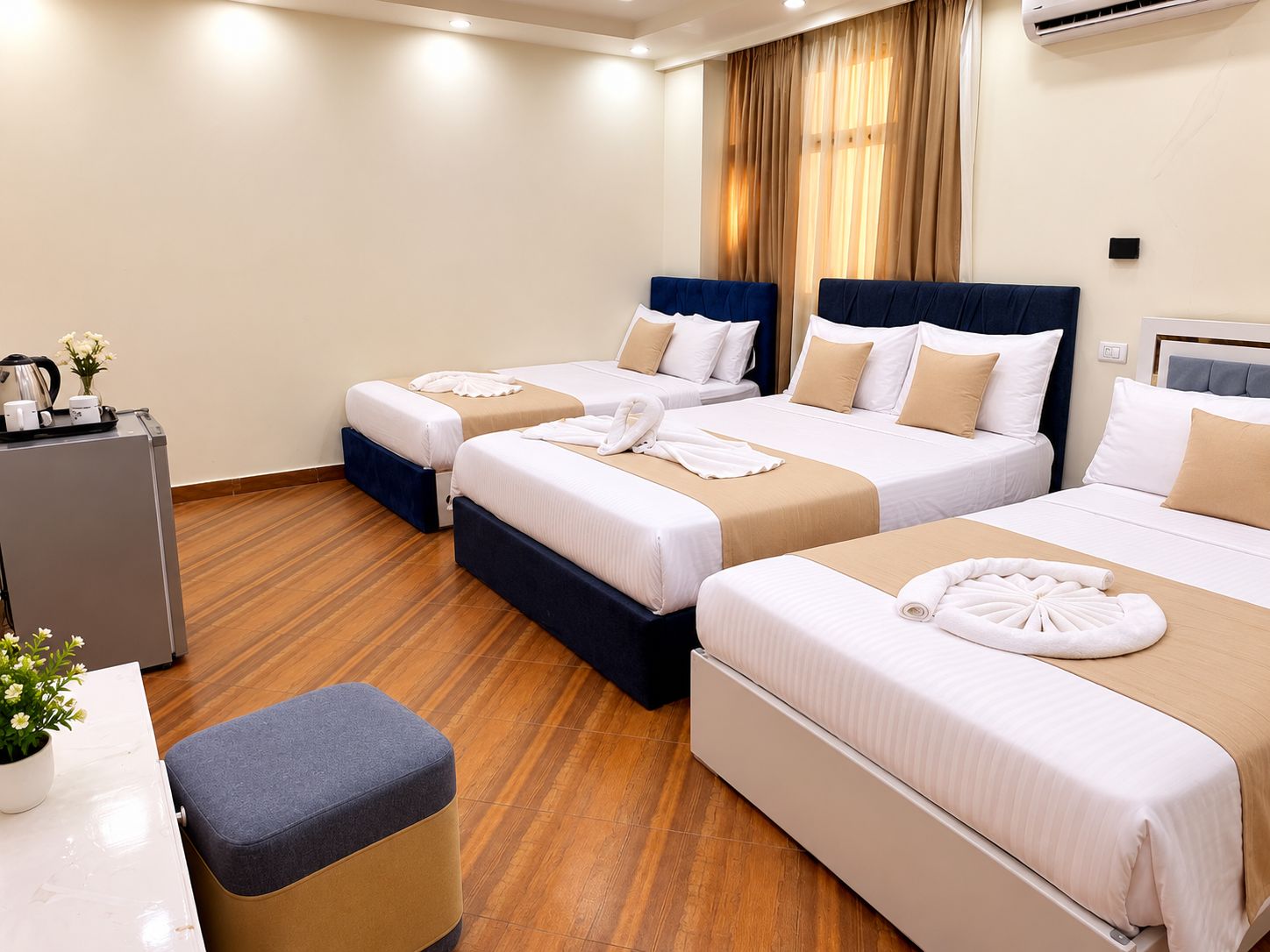 A hotel room with three beds, a desk, and a coffee station.