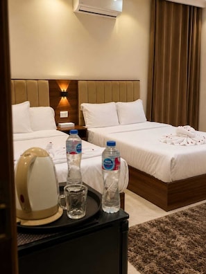 Habitación de hotel con dos camas, una mesita de noche con hervidor, botellas de agua y una bandeja.
