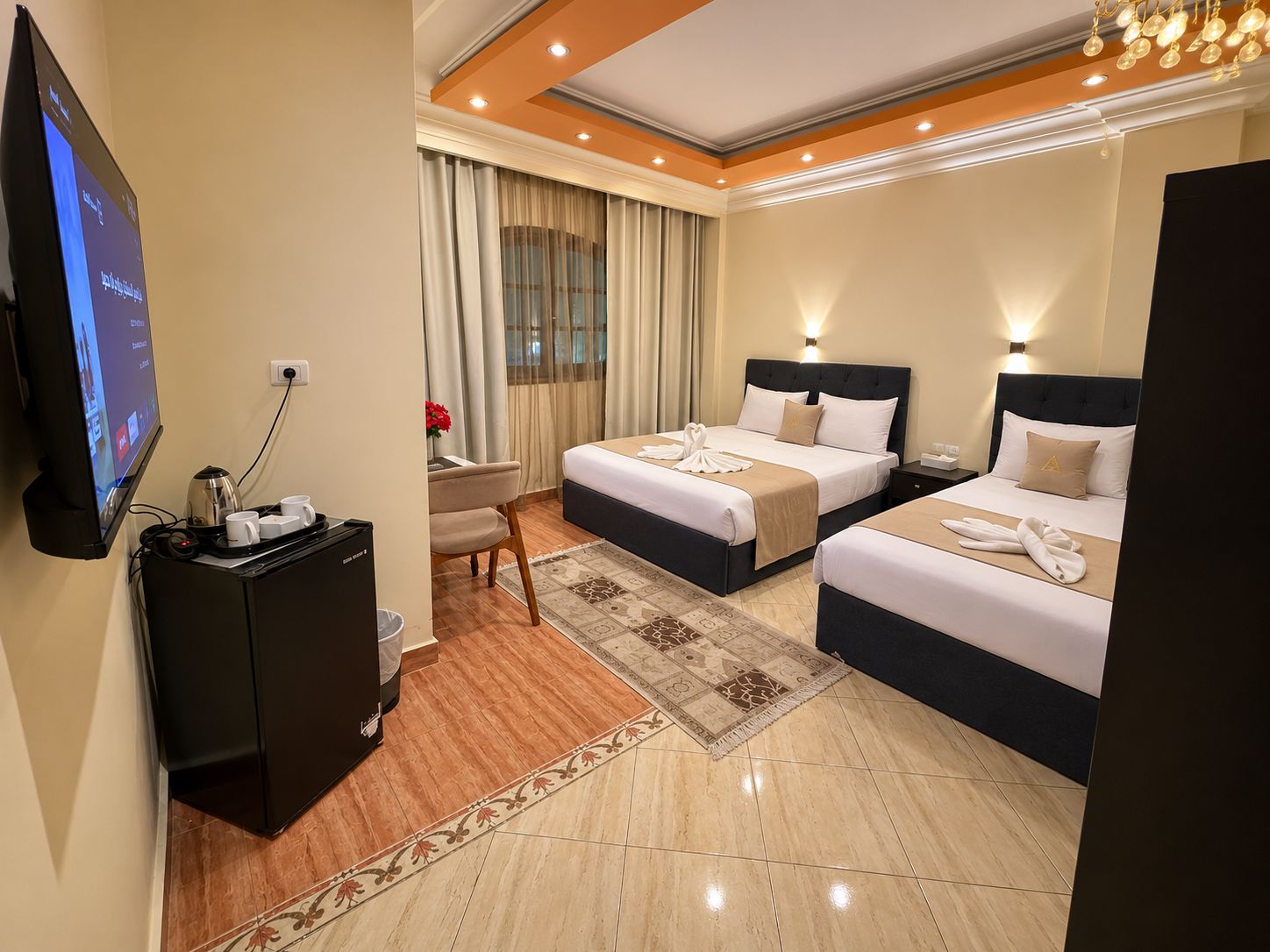 A hotel room with two beds, a desk with a computer and coffee maker, a TV, and a large window with curtains.