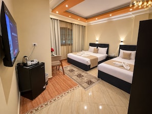 A hotel room with two beds, a desk with a computer and coffee maker, a TV, and a large window with curtains. - Pyramids Kingdom RZ Hotel (Giza)