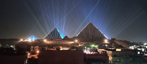 A large, illuminated structure with triangular shapes and a series of lights. - Queens Isis Pyramids View (Giza)