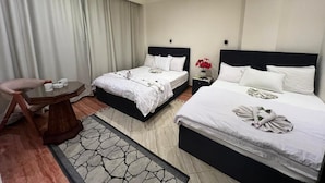 A hotel room with two beds, a small table, a chair, and a nightstand with a vase of flowers. - Pyramids Kingdom RZ Hotel  (Giza)