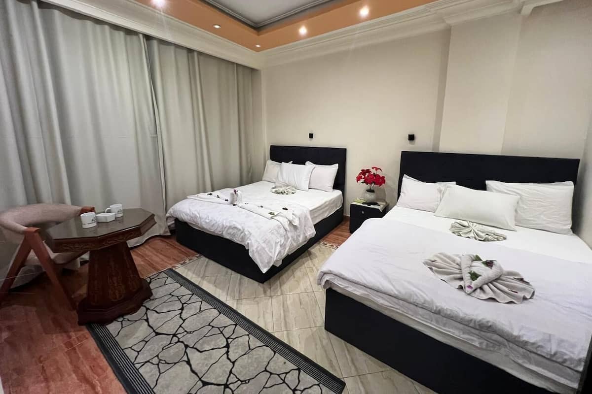 Une chambre d’hôtel avec deux lits, une petite table, une chaise et une table de chevet ornée d’un vase de fleurs.