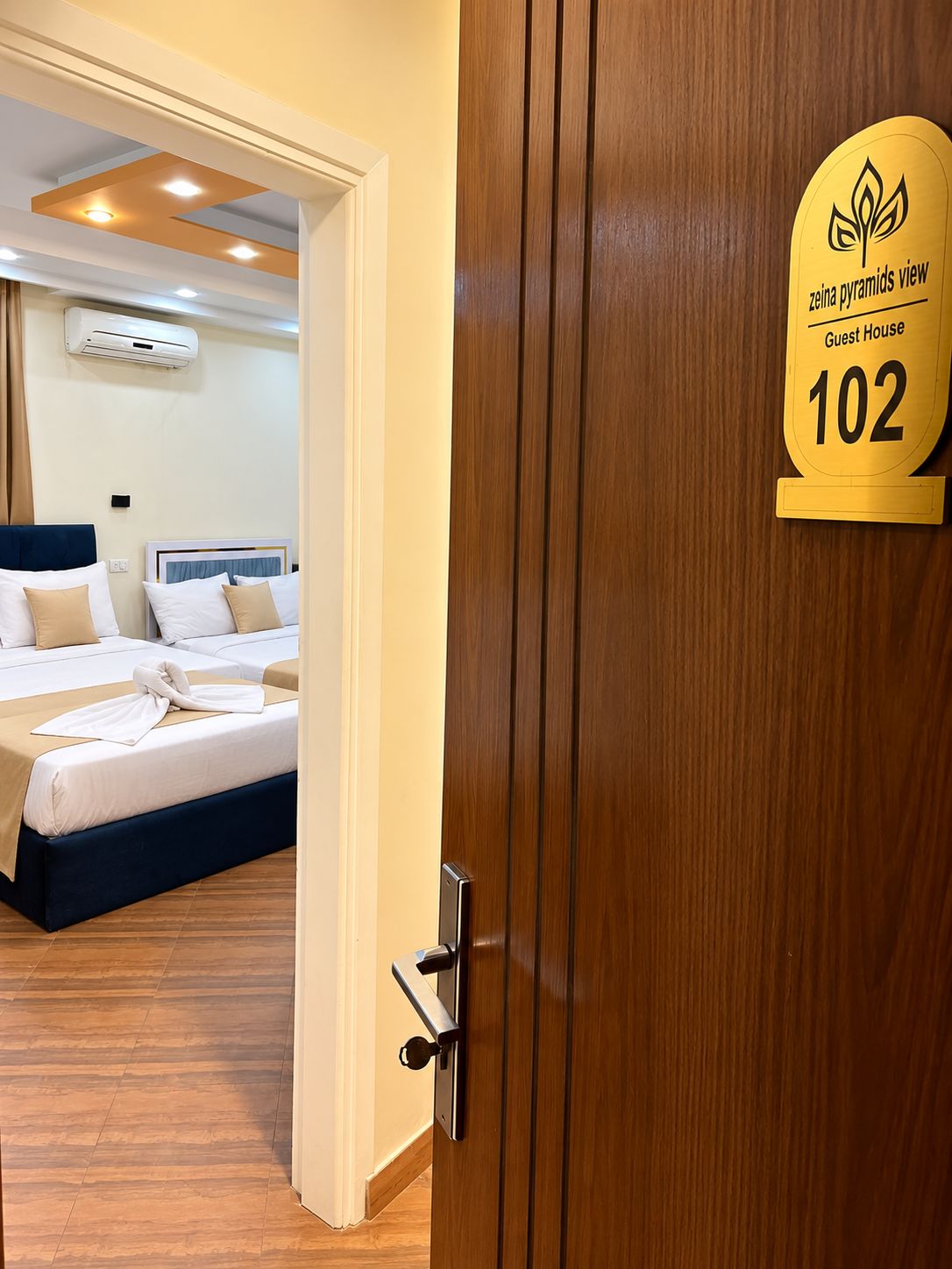 A hotel room with a bed, a bedside table, and a door with a sign indicating room number 102.