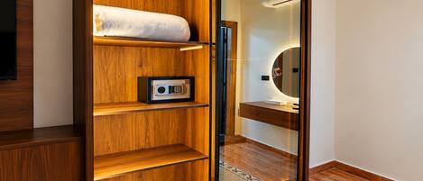 A wooden wardrobe with a mirror, a safe, and a shelf with a rolled-up towel.
