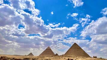 Une vue des pyramides, avec un ciel dégagé et quelques nuages.
